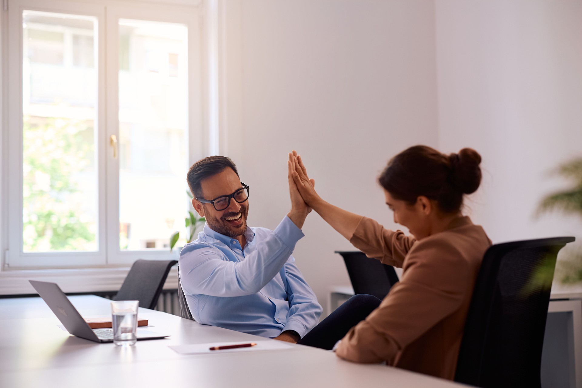Happy coworkers giving high-five while working in the office.