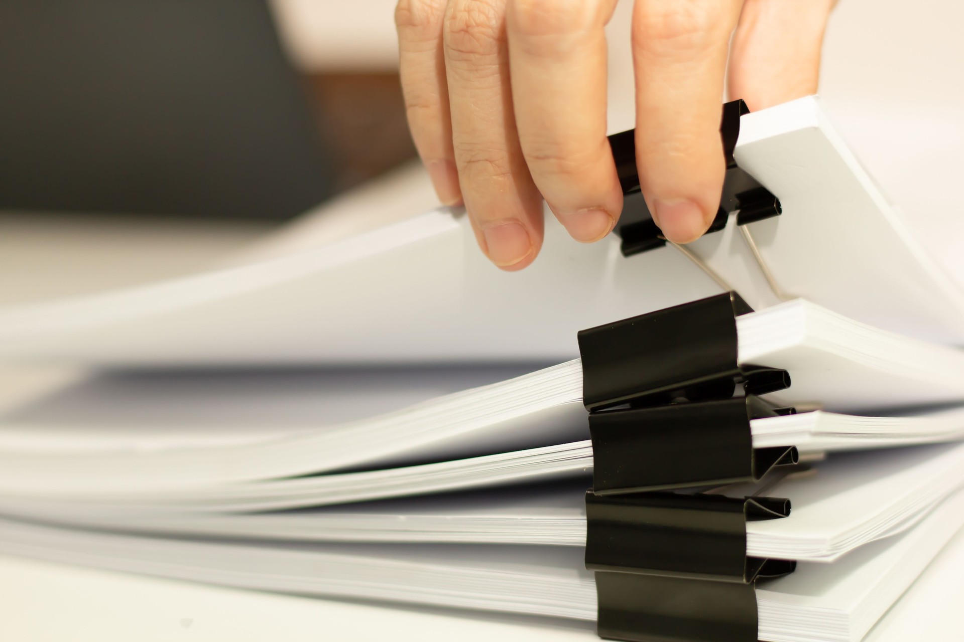 Close-up of woman hand pick up stack of report papers document with paper clip and laptop. Business, and education concept.